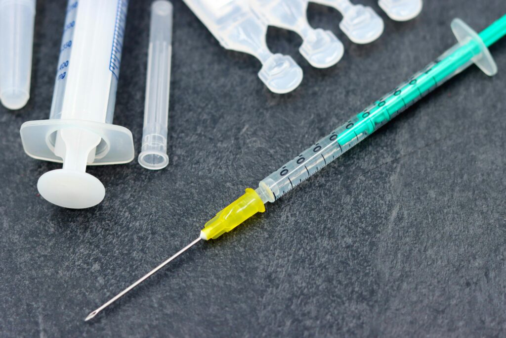 Close-up of medical syringes and needle components scattered on a dark surface, ready for use.
