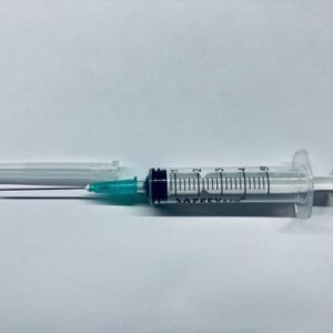 Disposable syringe with a green needle hub and exposed needle on a white surface