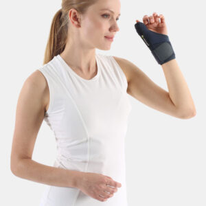 Woman in a white sleeveless top wearing a dark wrist brace on her right hand, raised as if ready to flex.