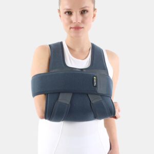 Woman wearing a blue shoulder/arm immobilizer (sling) across her chest against a white background with a calm expression.