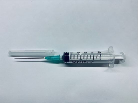 Disposable syringe with a green needle hub and exposed needle on a white surface