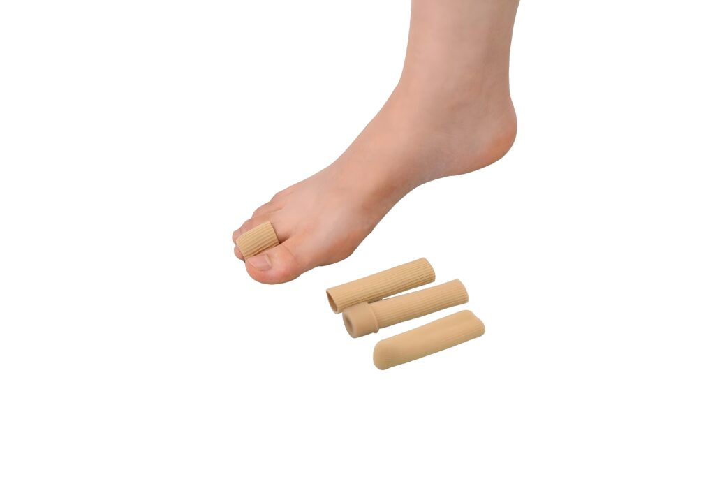 Close-up of a bare foot wearing beige silicone toe caps on several toes, with extra toe sleeves nearby.