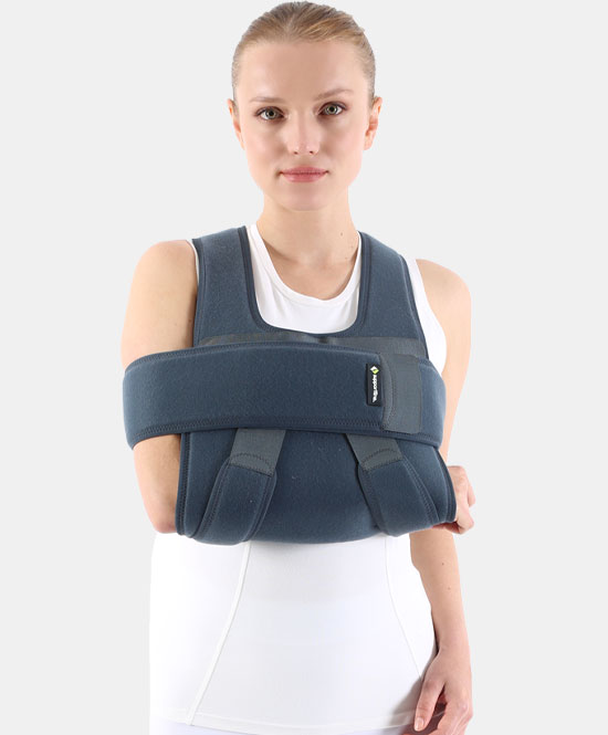 Woman wearing a blue shoulder/arm immobilizer (sling) across her chest against a white background with a calm expression.